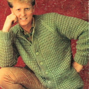 May include: A green knitted cardigan with a button-up front. The cardigan has a textured stitch pattern and is being worn by a person with brown hair.