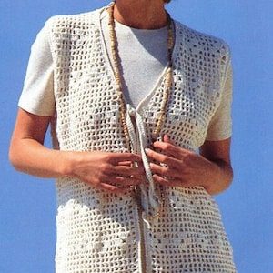 May include: A white crocheted vest with a tie closure. The vest has a delicate openwork pattern and is worn over a white t-shirt.