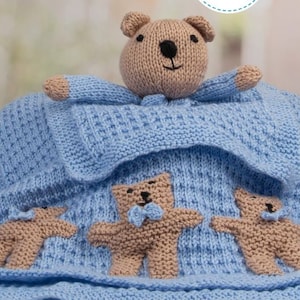 Può includere: Una coperta per neonati lavorata a maglia blu chiaro con tre orsetti marroni e una testa di orsetto. La coperta ha un motivo strutturato ed è realizzata in filato morbido. Gli orsetti hanno occhi neri e nasi marroni. La coperta è per un bambino.