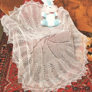 May include: A white crocheted baby blanket with a delicate lace pattern. The blanket is draped over a chair with a stuffed bunny toy sitting on top.