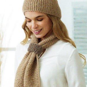 May include: A beige knitted hat and scarf set. The hat is a close-fitting beanie style. The scarf is long and rectangular, with a darker band detail. The set is made of a textured yarn, ideal for colder weather.