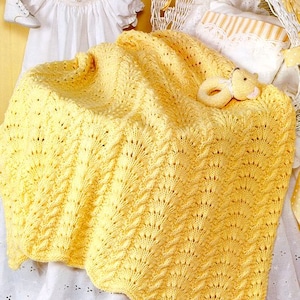 Pode incluir: Um cobertor de bebé amarelo de crochê com um padrão delicado e rendado. O cobertor está drapeado sobre uma cesta de vime branca e um lençol de berço branco.