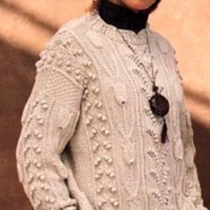 May include: A cream-coloured knitted jumper with a cable knit pattern and a textured design. The jumper has a round neckline and long sleeves.