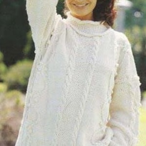 May include: A white knitted sweater with a cable knit pattern. The sweater has a loose fit and a high neckline.
