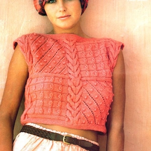 May include: A pink knitted sleeveless top with a cable knit design and a textured pattern. The top is cropped and has a wide neckline.