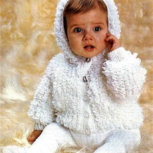 May include: A white knitted baby cardigan with a hood, featuring a textured, bobbly stitch. The cardigan has a button closure and is worn by a baby with brown hair.