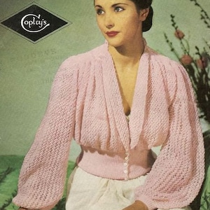 Könnte beinhalten: Ein rosa gestrickter Pullover mit V-Ausschnitt und langen Ärmeln. Der Pullover hat einen taillierten Oberkörper und eine lockere, fließende Passform in den Ärmeln. Der Pullover wird vorne mit kleinen weißen Knöpfen geschlossen.