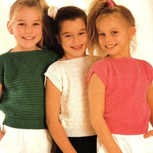May include: Three girls wearing sleeveless knitted tops in green, white, and pink. The girls are smiling and looking at the camera.
