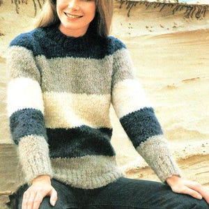 May include: A striped jumper with a crew neck in shades of blue, white, and grey. The jumper is made of a soft, fluffy yarn and has a relaxed fit.