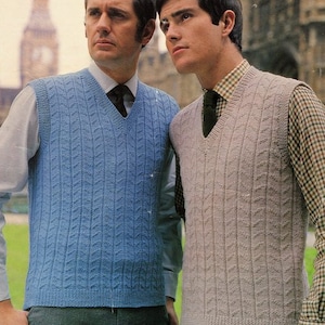 May include: Two men wearing knitted v-neck vests. The vest on the left is blue and the vest on the right is beige.
