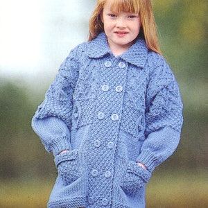 Op de afbeelding: Een lichtblauwe gebreide cardigan met een dubbele knoopsluiting en zakken. De cardigan heeft een kabelbreipatroon en wordt gedragen door een kind.