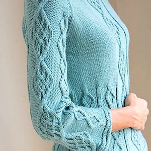 Könnte beinhalten: Hellblauer Strickpullover mit aufwendigen Zopfmustern an Ärmeln und Körper. Der Pullover hat einen Rundhalsausschnitt und lange Ärmel mit ausgestellten Manschetten. Das Design zeigt einen strukturierten, handgefertigten Look.