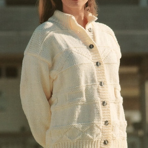 May include: A white knitted cardigan with a button-up front and a textured pattern. The cardigan is worn over a floral print skirt.