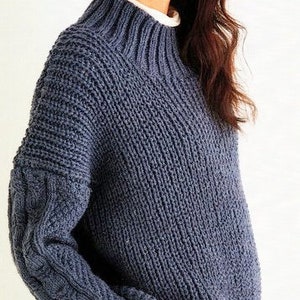 May include: A blue knitted sweater with a high neck and cable knit detail on the sleeves.