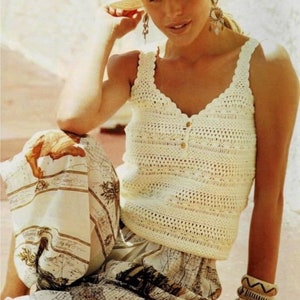 Puede incluir: Un top blanco de crochet con cierre de botón y escote festoneado. El top se lleva con un sombrero blanco y una falda estampada.