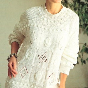 May include: A white knitted sweater with a geometric pattern and bobbles. The sweater has a crew neck and long sleeves.