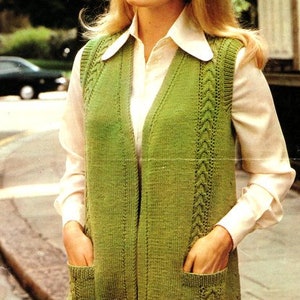 Könnte beinhalten: Eine grüne Strickweste mit Zopfmuster und Taschen. Die Weste ist vorne offen und hat einen V-Ausschnitt. "Double Knitting 38-44 in." steht oben im Bild.