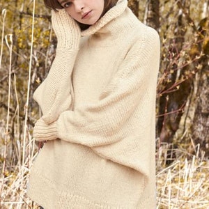 May include: A cream-coloured knitted jumper with a turtleneck and long sleeves. The jumper has a relaxed fit and a slightly oversized silhouette.