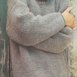 May include: A gray turtleneck sweater with a loose fit and a ribbed texture. The sweater is made of a soft, warm material and is perfect for layering.