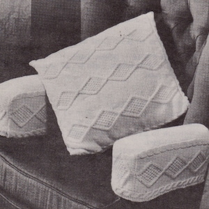 Peut inclure: Trois housses de coussin blanches en tricot avec un motif en losange. Les housses sont sur un canapé brun foncé.