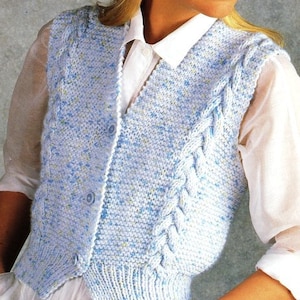 Może przedstawiać: Jas bez rękawów w jasnoniebieskim kolorze, wykonany z dzianiny z warkoczowym wzorem i zapinany na guziki. Kamizelka ma wzór w kropki i jest noszona na białej koszuli zapinanej na guziki.