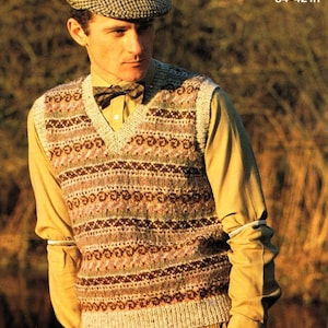 May include: A brown, white, and green patterned knitted vest with a V-neck. The vest has a brown bow tie and is worn over a light brown button-down shirt. The text "86-107 cm 34-42 in" is visible in the top right corner of the image.