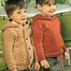 Op de afbeelding: Twee kinderen dragen gebreide truien. Het kind links draagt een beige trui met een kabelbreipatroon en een capuchon. Het kind rechts draagt een rode trui met een capuchon. Beide kinderen lachen.
