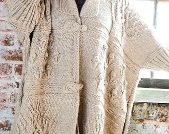 Könnte beinhalten: Ein beigefarbener Strickcardigan mit einem Zopfmuster und floralen Verzierungen. Der Cardigan hat einen Schalkragen und einen Knopfverschluss.