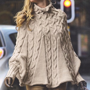 May include: A beige cable knit poncho with a high neck and long sleeves. The poncho is made of a soft, warm material and has a relaxed fit.