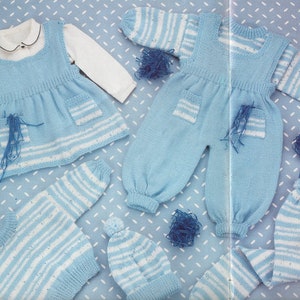 Pode incluir: Um conjunto de roupas de bebé de malha em azul e branco listrado. O conjunto inclui um vestido, um macacão, um chapéu e um par de luvas.
