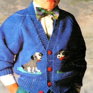 May include: A blue knitted cardigan with a V-neck and button closure. The cardigan features two embroidered dog designs on the front. The cardigan is worn by a child wearing a white shirt and a plaid bow tie.