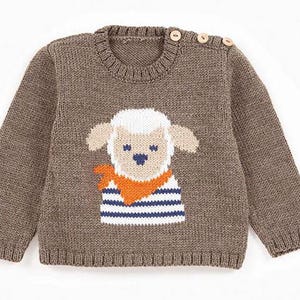 Op de afbeelding: Een bruine gebreide trui met een schapenmotief op de voorkant. Het schaap heeft een wit gezicht, beige oren en een blauwe neus. Het draagt een oranje sjaal en een blauw-wit gestreept shirt. De trui heeft houten knopen op de schouder.
