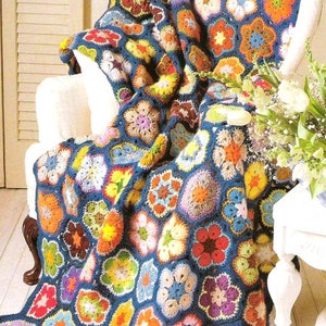 May include: A crocheted blanket with a blue background and colorful flower designs. The blanket is draped over a white armchair with a floral arrangement on a white table.