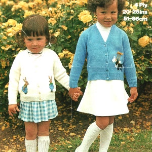 May include: Two young girls wearing knitted cardigans with embroidered bunny and dog designs. The girl on the left is wearing a white cardigan with two bunnies, a blue and white plaid skirt, and white socks. The girl on the right is wearing a blue cardigan with a dog, a white skirt, and white socks. The text on the image reads "4 Ply 20-26ins 51-66cm".