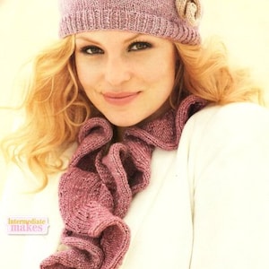 May include: A knitted hat and scarf set in a dusty rose color. The hat has a flower accent and the scarf has a ruffled design. The image shows a close-up of the hat and scarf.