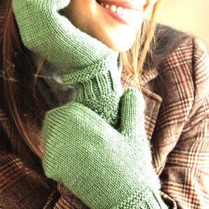 May include: A woman wearing a green knitted mitten set. The mittens are a light shade of green and have a textured knit pattern. The woman is wearing a brown plaid jacket.