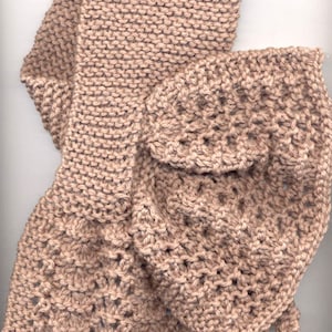 Könnte beinhalten: Ein gestrickter Schal in hellbrauner Farbe mit einem einfachen Stichmuster auf der einen Seite und einem komplizierteren Muster auf der anderen.