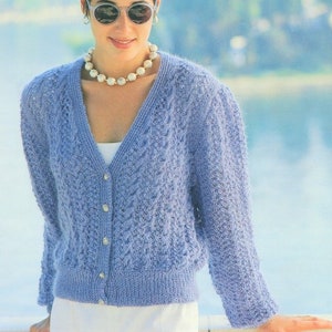 Könnte beinhalten: Ein hellblauer Strickcardigan mit V-Ausschnitt und Knopfleiste. Der Cardigan hat ein zartes Spitzenmuster und wird über einem weißen Oberteil getragen.