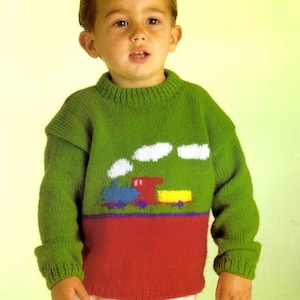 May include: A green knitted sweater with a red bottom and a white train with clouds design. The sweater has long sleeves and a crew neck.