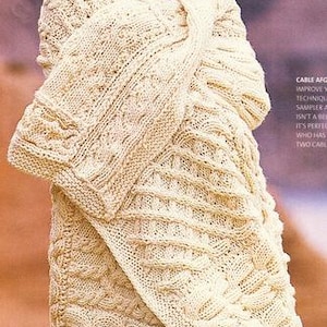May include: A woman wearing a cream-coloured, cable-knit wrap. The wrap features intricate patterns and textures, with a long, flowing design. The word "Technique" is visible in the upper left corner.