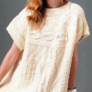 May include: A white knitted sweater with a cable knit design and a short sleeve. The sweater has a loose fit and a round neckline.