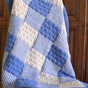 Puede incluir: Una manta de bebé tejida con un diseño de patchwork en tonos azules y crema. La manta está hecha con diferentes patrones de punto, incluyendo rayas y un patrón de cesta.
