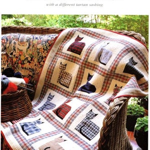 May include: A handmade quilt featuring a cream background with a grid pattern and cat appliqués in various tartan fabrics. The quilt is draped over a wicker chair, showcasing its design and craftsmanship.