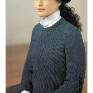 May include: A dark blue knitted sweater with a round neckline. The sweater is worn by a person wearing a white collared shirt and a black hat.