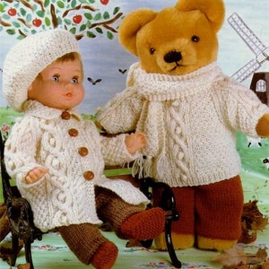 May include: A knitted doll wearing a white sweater and brown pants sits next to a brown teddy bear wearing a white sweater and brown pants. Both are sitting on a wooden bench.