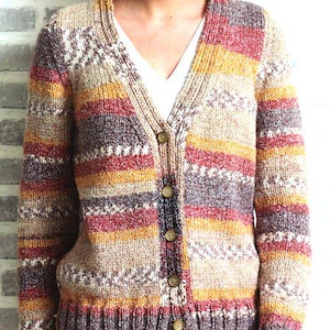 Puede incluir: Un cárdigan de punto multicolor con cuello en V y cierre de botones. El suéter presenta rayas horizontales en tonos beige, rojo, amarillo y marrón. Los puños y el dobladillo son de color marrón oscuro. El suéter se usa sobre una camiseta blanca.