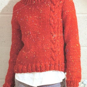 May include: A red knitted jumper with a cable knit design on the shoulder and a speckled texture throughout.