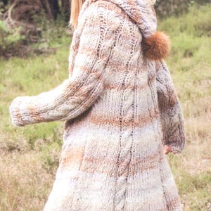 May include: A long, hooded knit coat in cream, brown, and tan stripes. The coat features a cable knit design down the front and sleeves, with a brown pom-pom on the hood. The coat is knee-length.