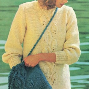 May include: A woman wearing a white knitted sweater with a cable knit design and a blue knitted hat. She is carrying a blue knitted bag with a drawstring closure.