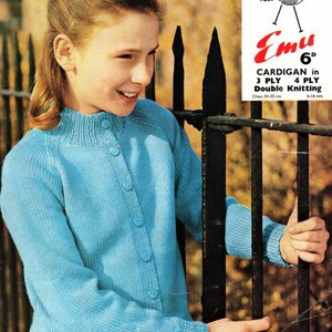 Puede incluir: Una niña lleva un cárdigan azul claro con botones. El cárdigan está tejido y tiene un cuello de canalé. La niña está de pie frente a una valla de metal negro. La imagen es de un patrón de tejido vintage.